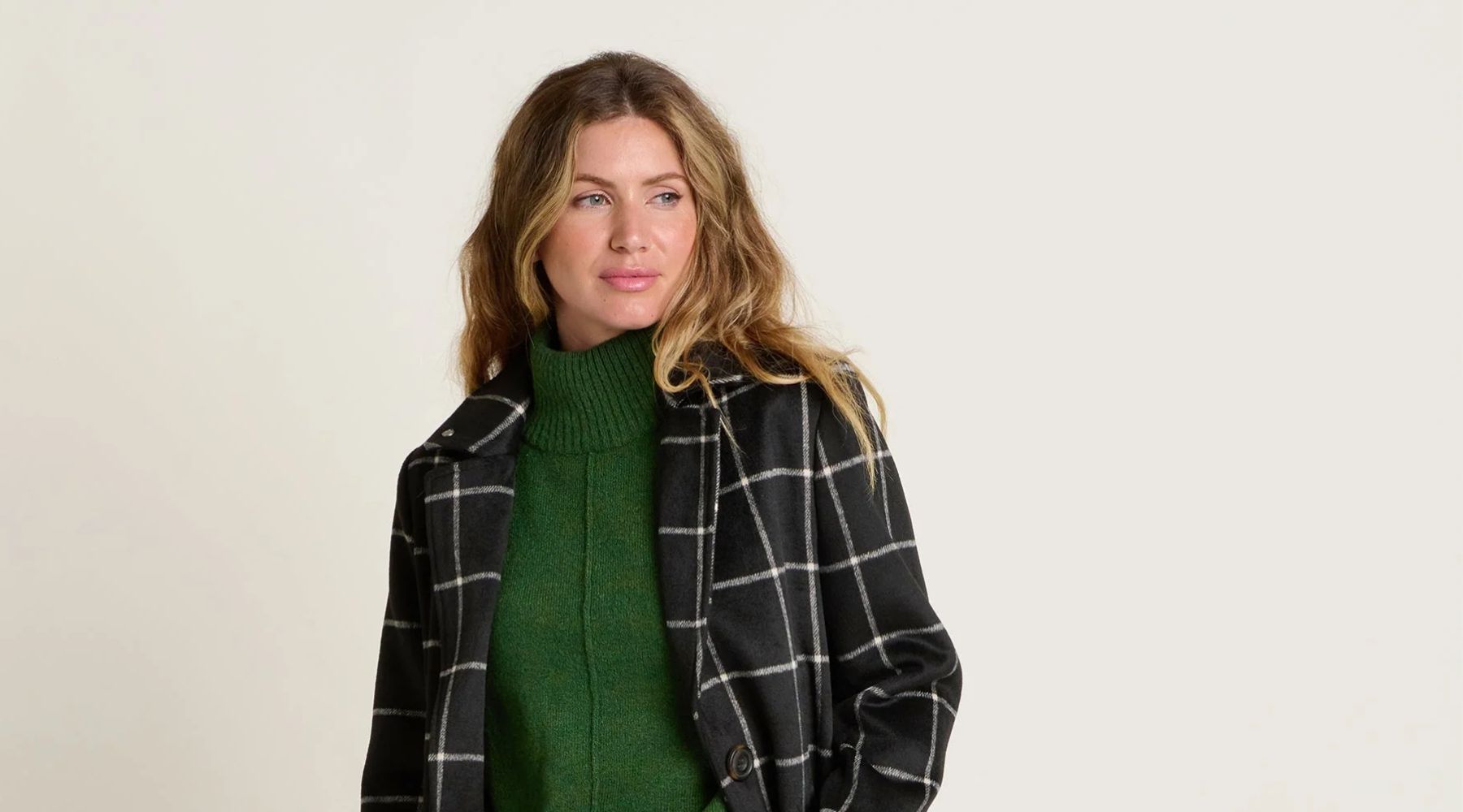 Female model in a dark green knitted jumper and a black and white long coat