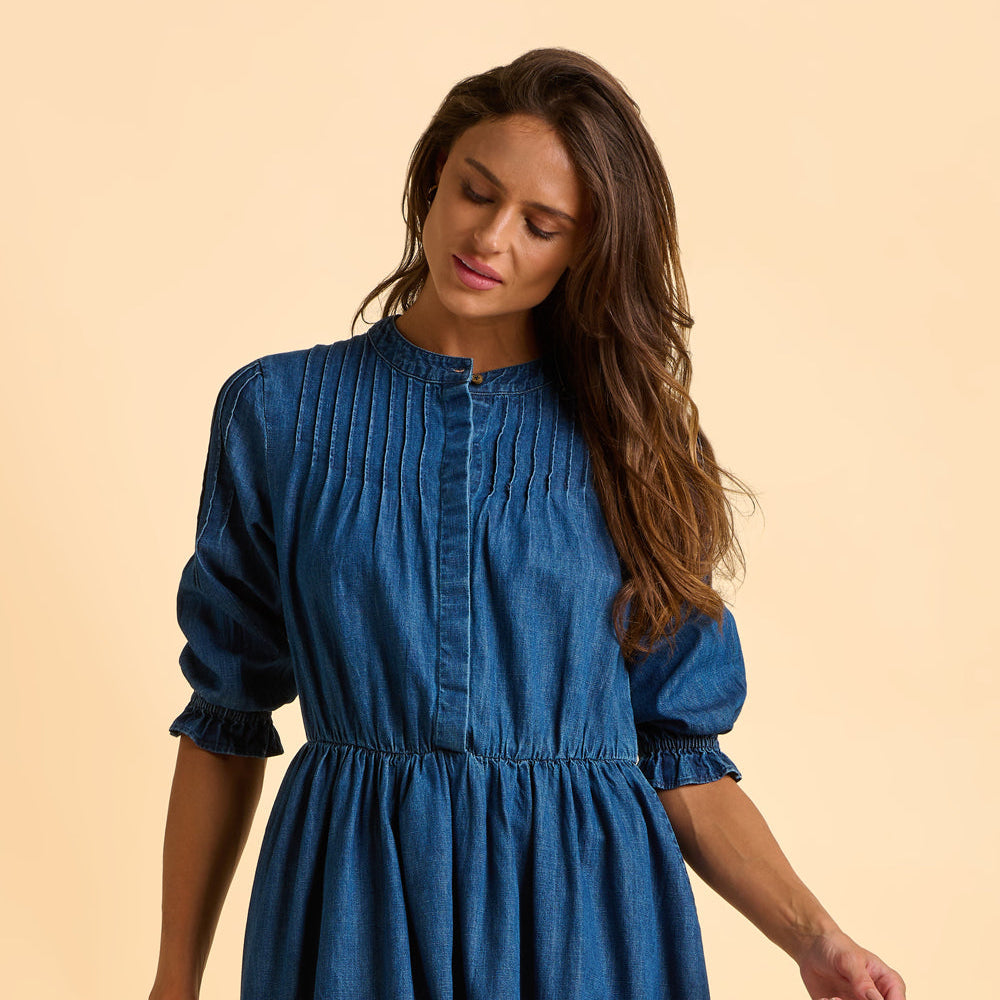 Female model wearing a blue denim dress against a beige background