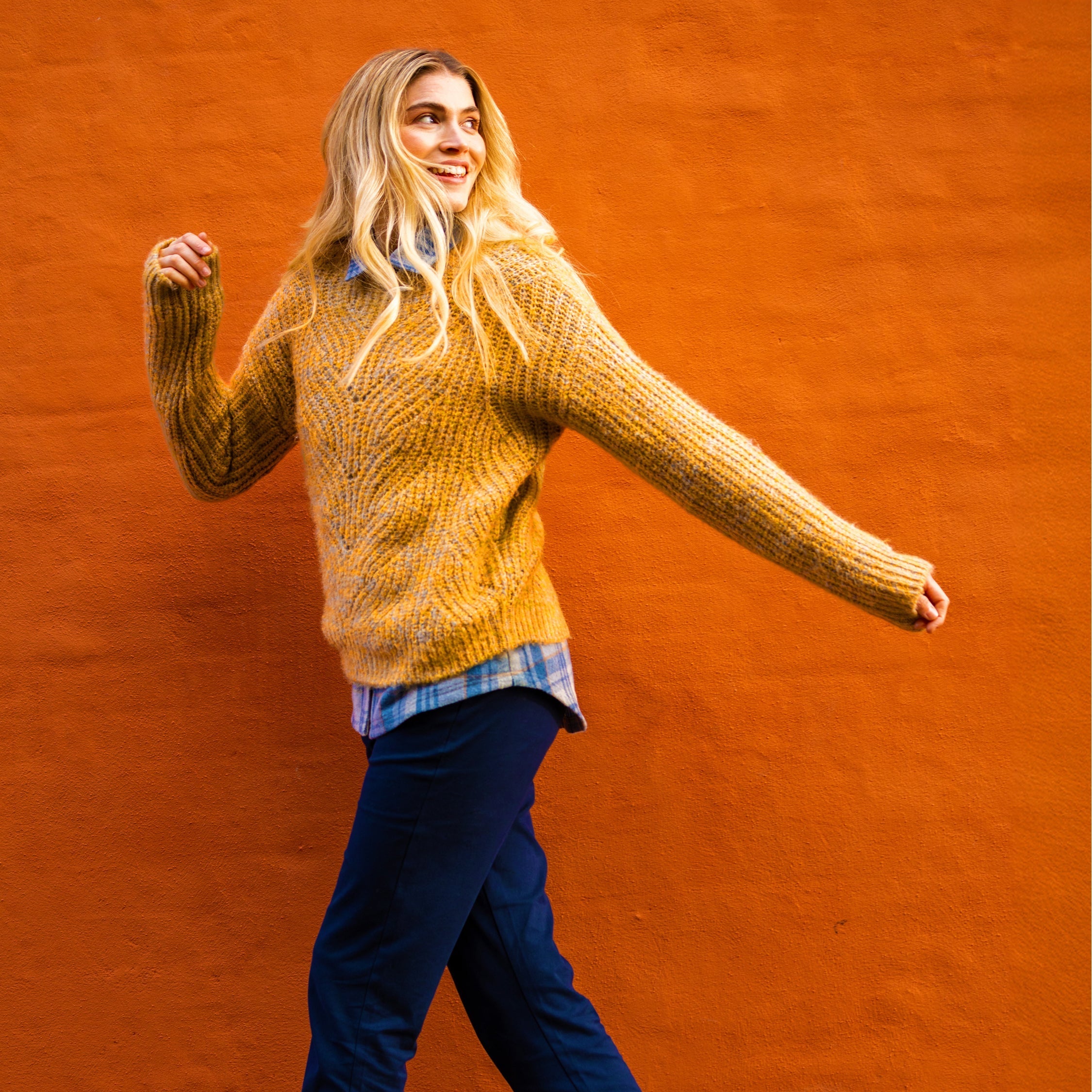 Female model wearing a Brakeburn jumper walking in front of a orange wall.