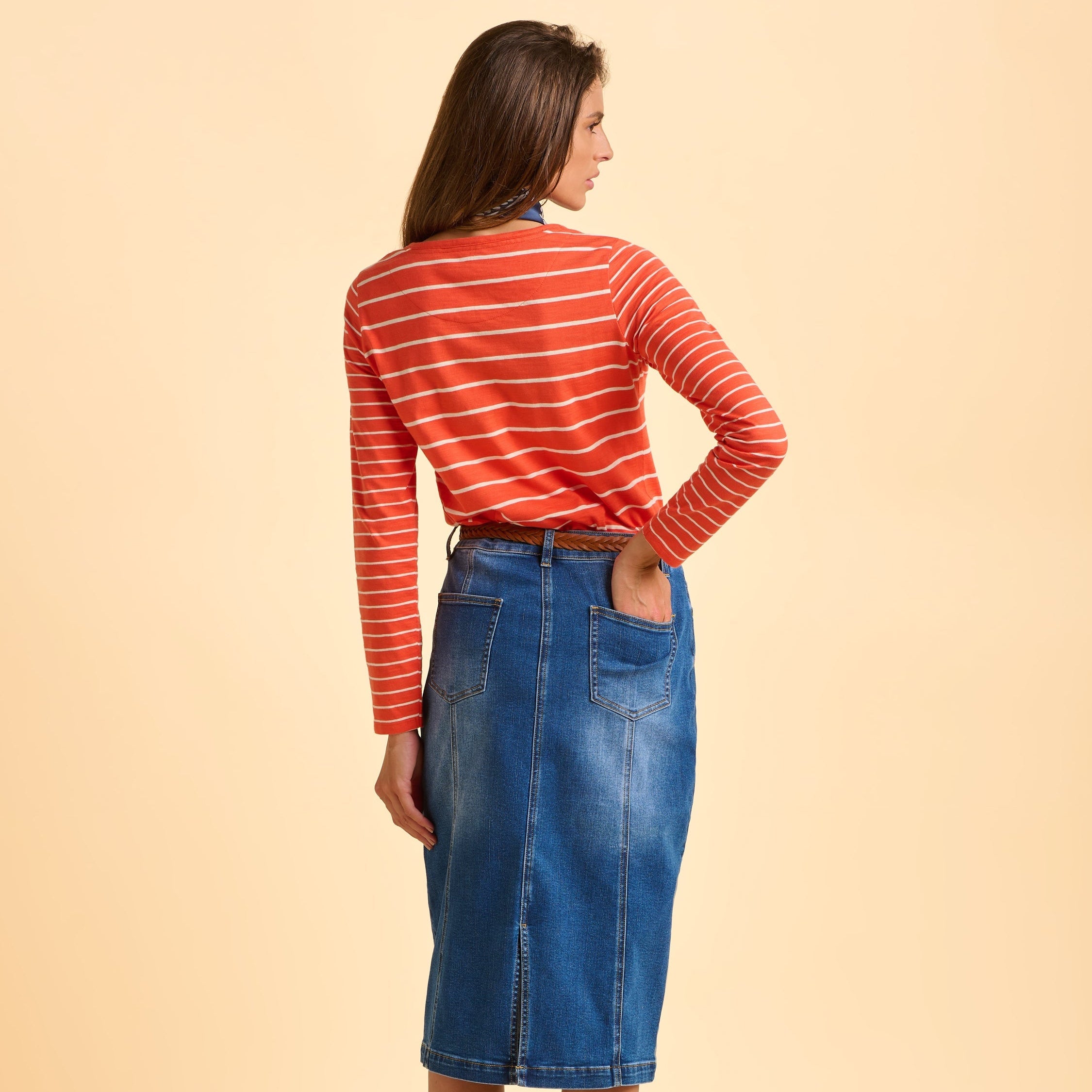 Female model wearing a red striped shirt and blue denim skirt on a beige background