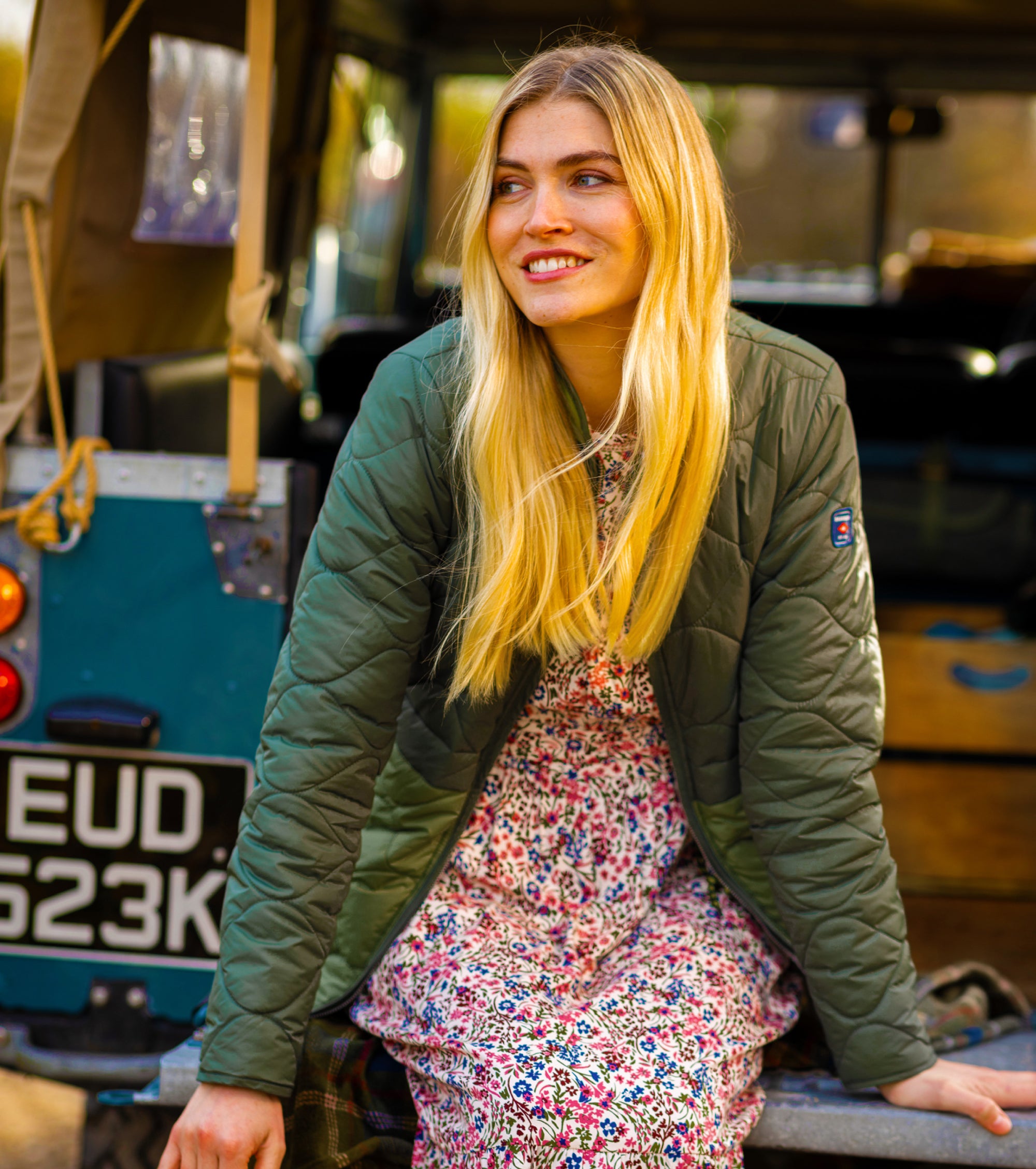 Woman in a floral dress and green jacket sitting in a truck