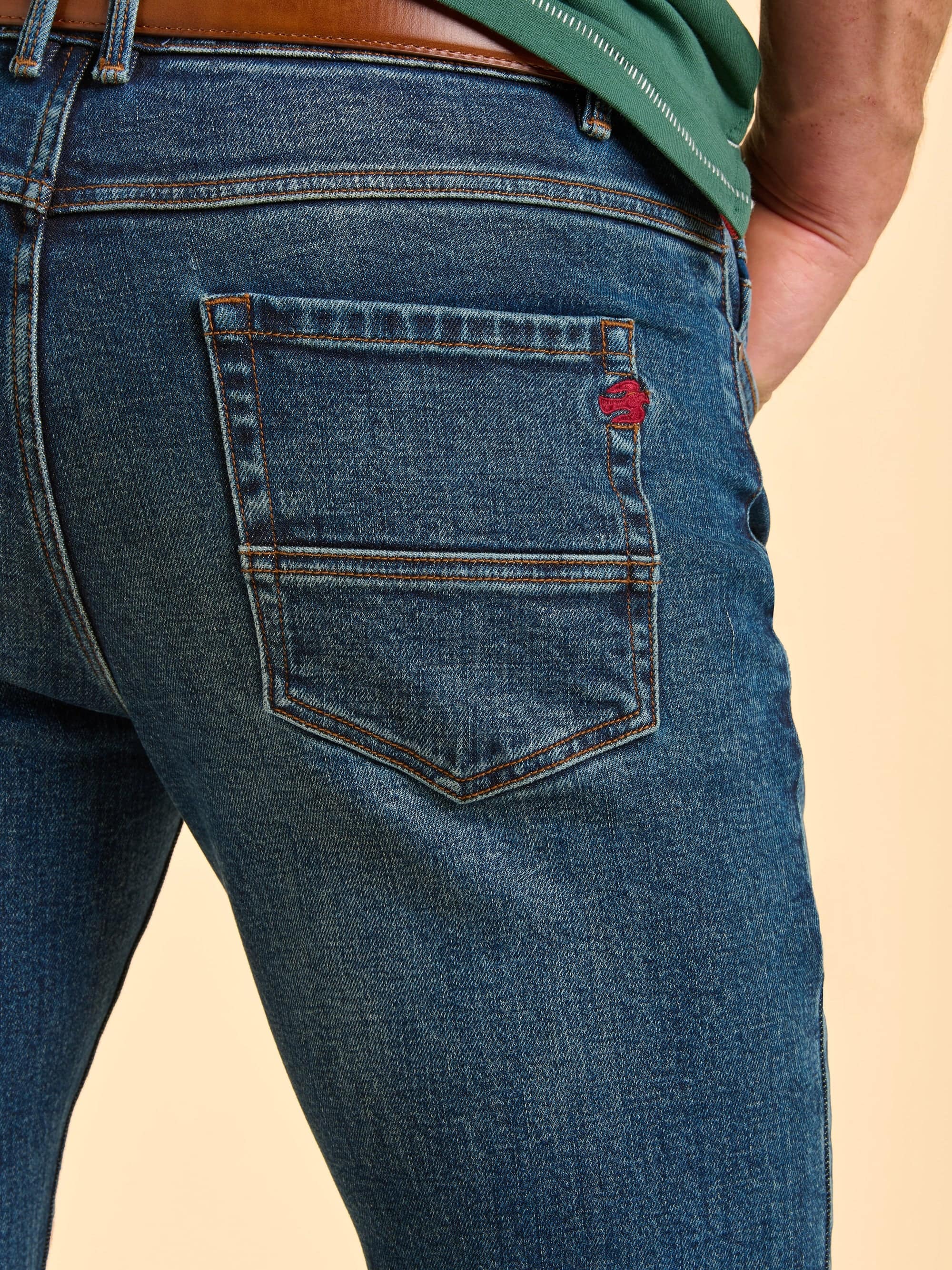 Close-up of the back of blue jeans with a Brakeburn logo embroidered on the back pocket.