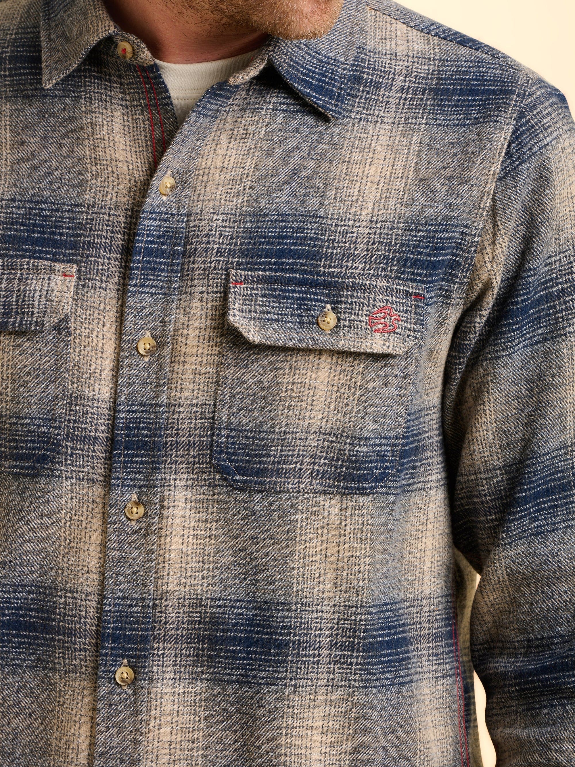 Close-up of a blue plaid check shirt with a red Brakeburn logo embroidered on the pocket.