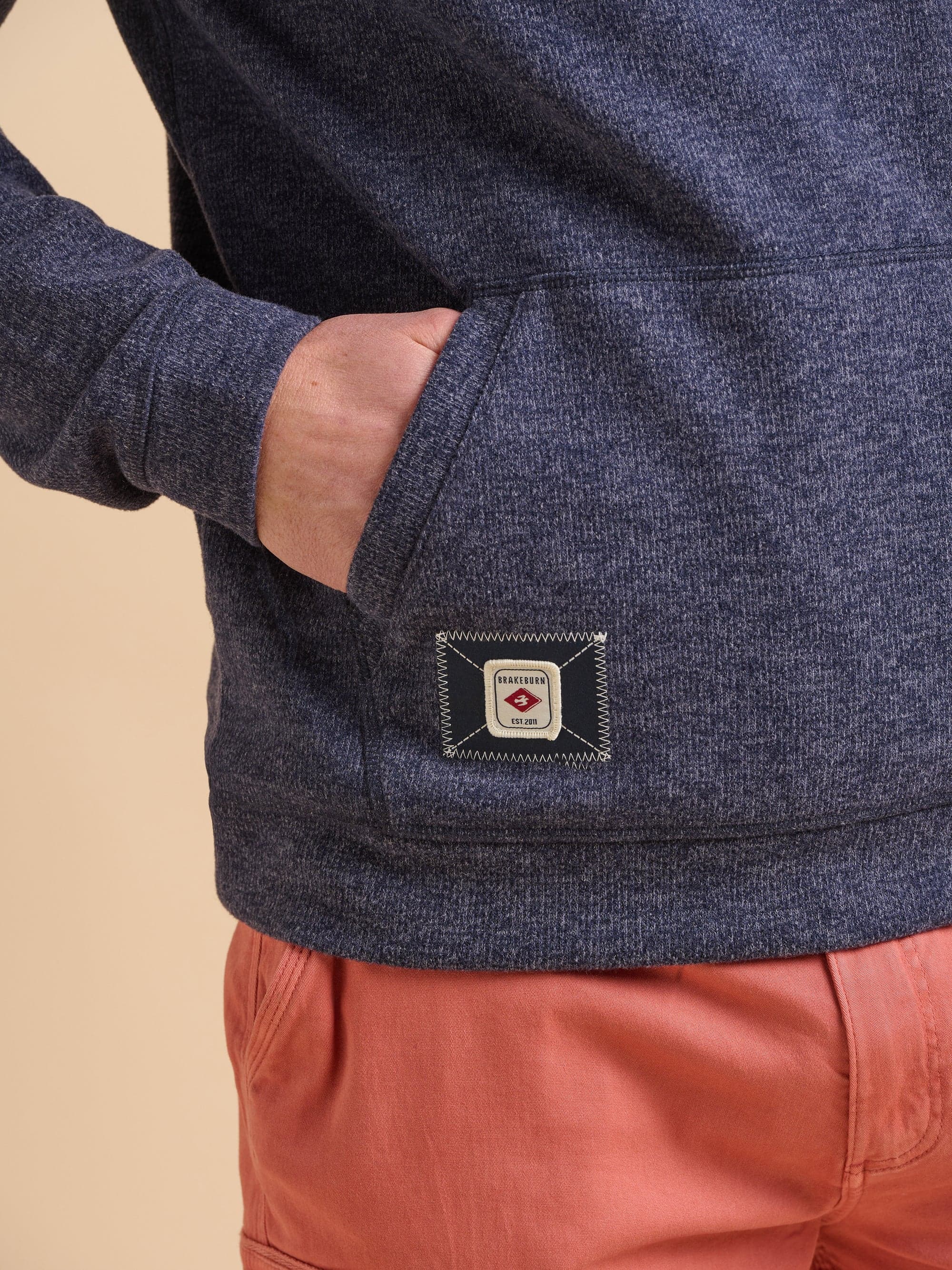 Navy blue marl hoodie with a Brakeburn logo on the pocket in front of a beige background.