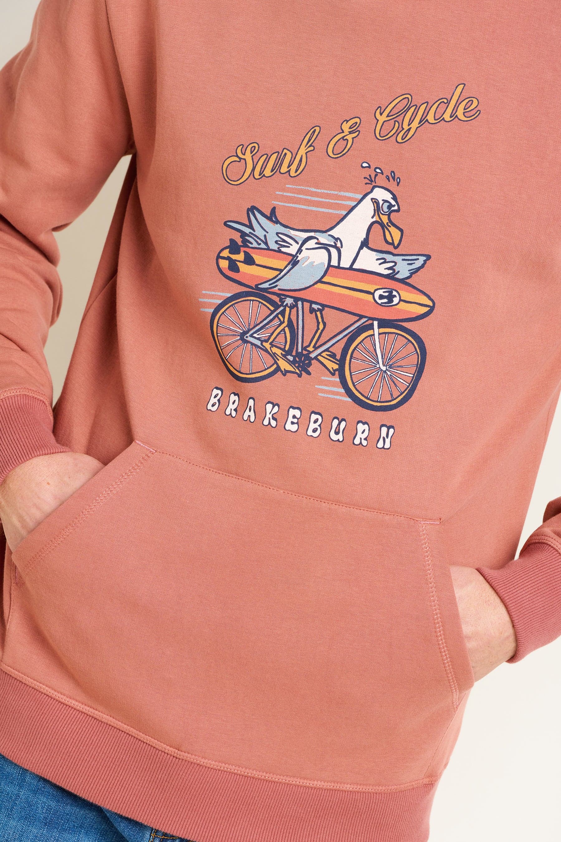 Mens red hoodie with a graphic design of a seagull on a bike and text 'Surf & Cycle Brakeburn'.