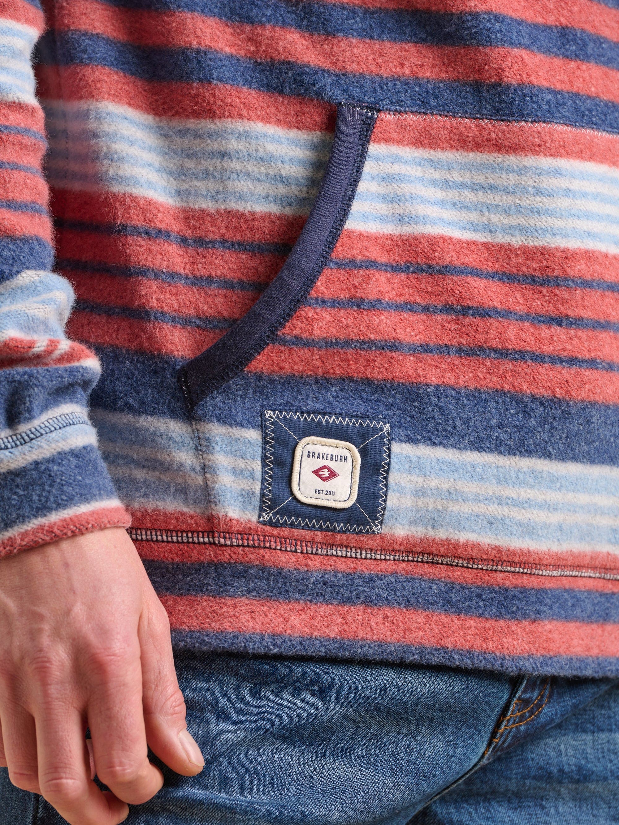 Close up of a red and blue striped hoodie with a Brakeburn label embroidered on the pocket.