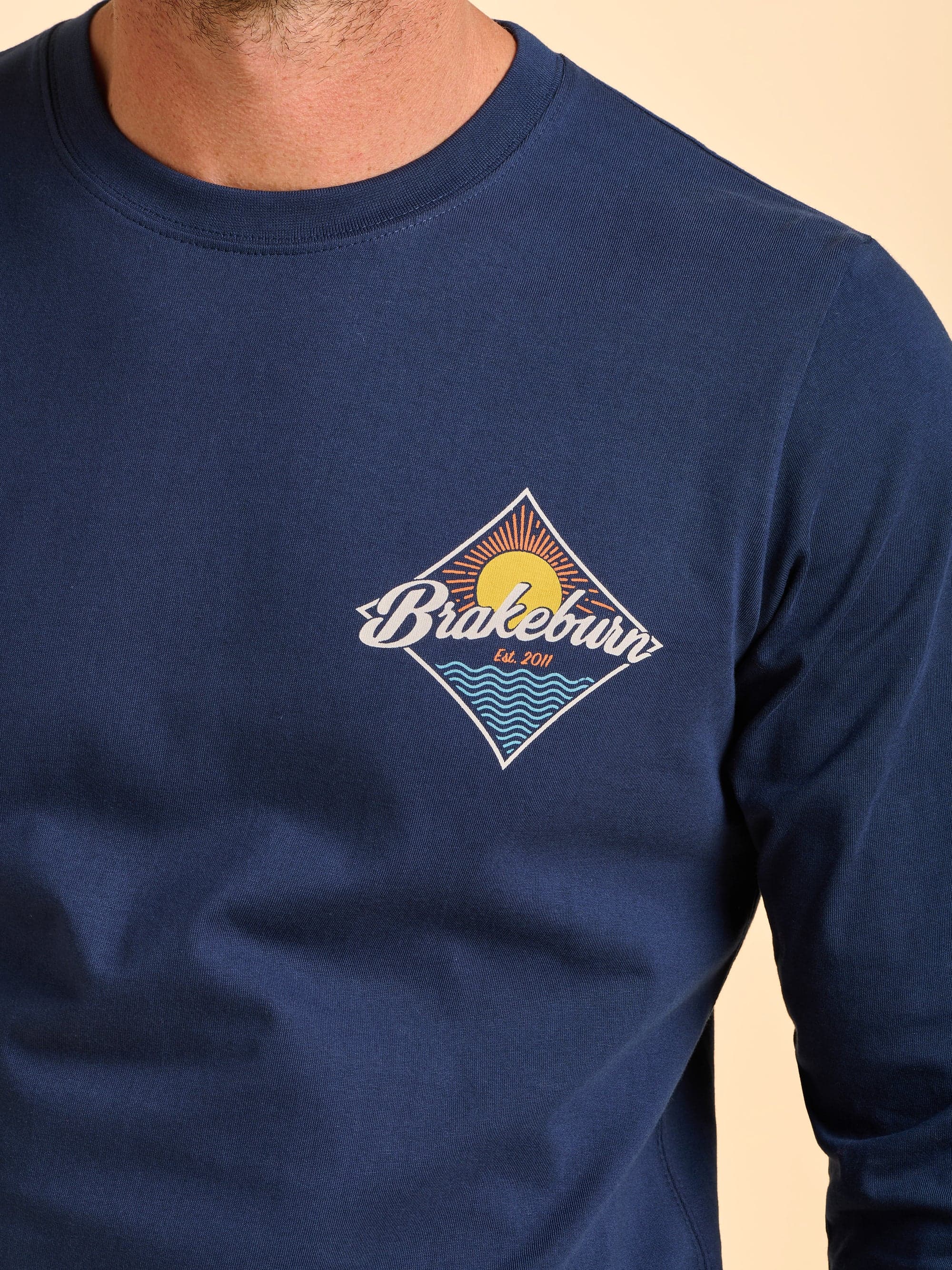 Man wearing a navy blue Brakeburn long sleeve T-Shirt with a Brakeburn graphic in the top left.