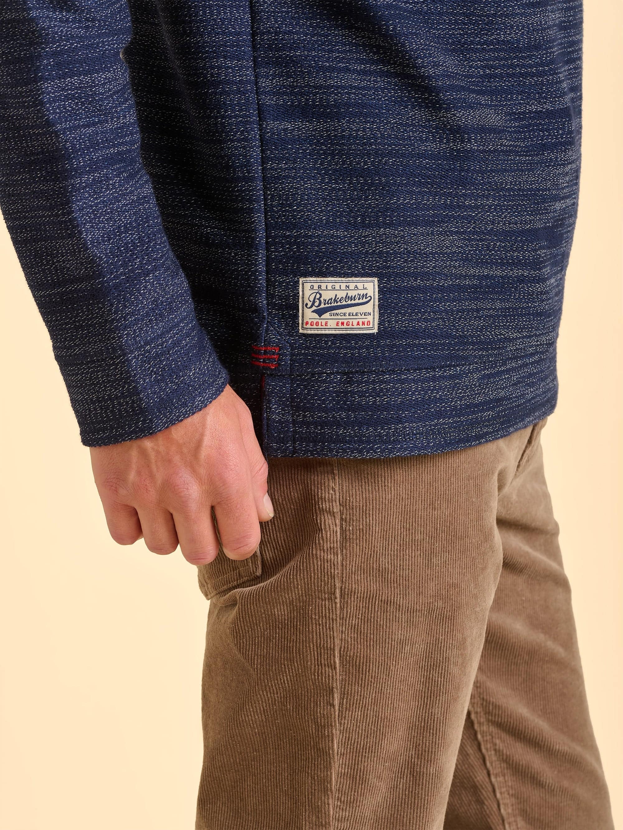 Close-up of a man wearing a blue textured jacket with a Brakeburn logo on the bottom right.