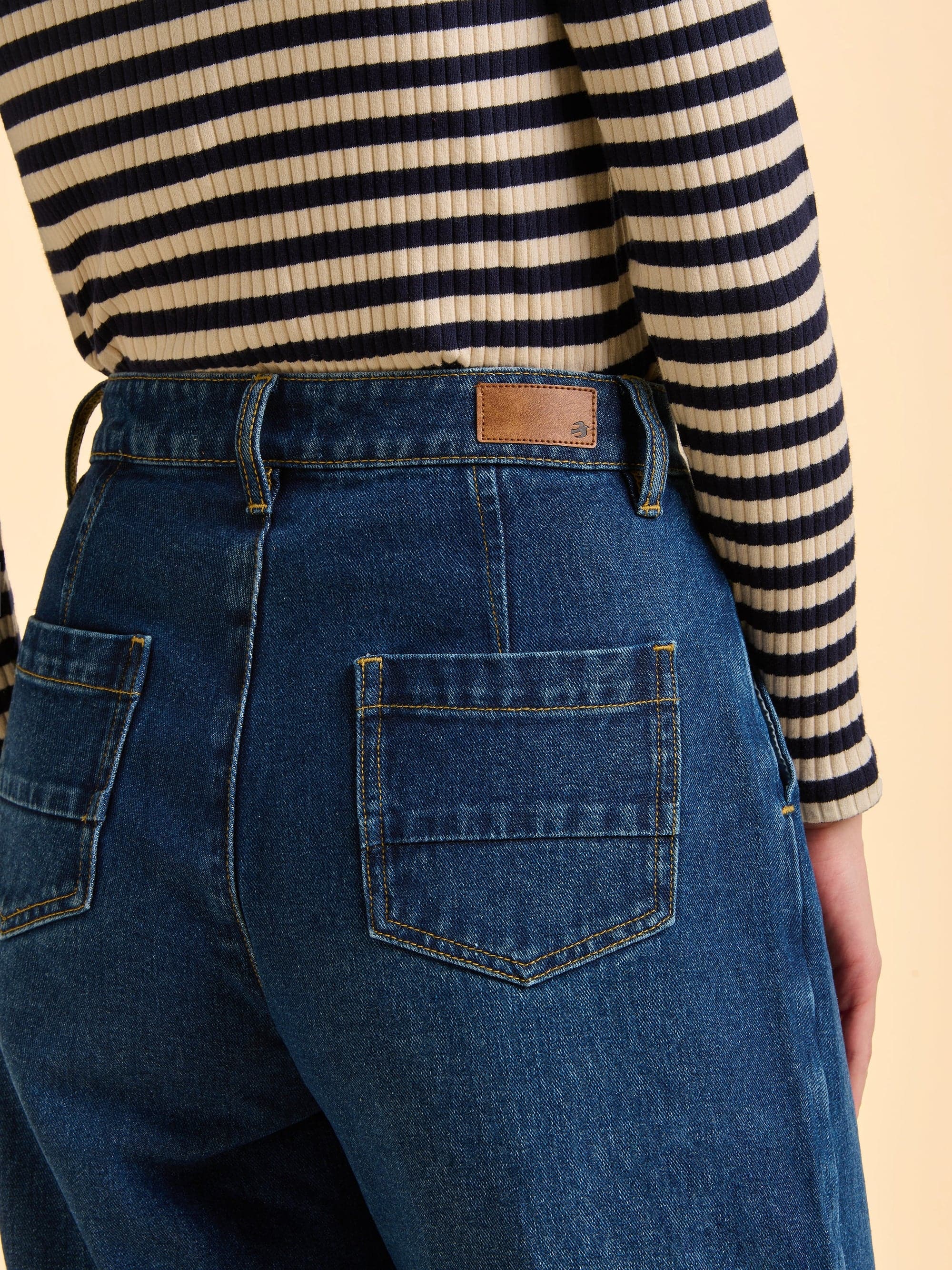 Woman wearing the blue bodhi jeans and a striped sweater with a beige background.
