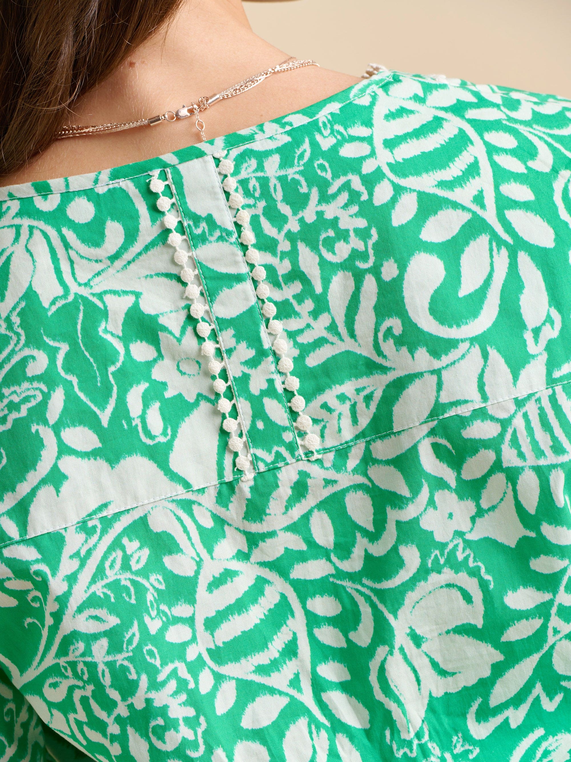 The back of a green and white patterned blouse with a close-up of a necklace.