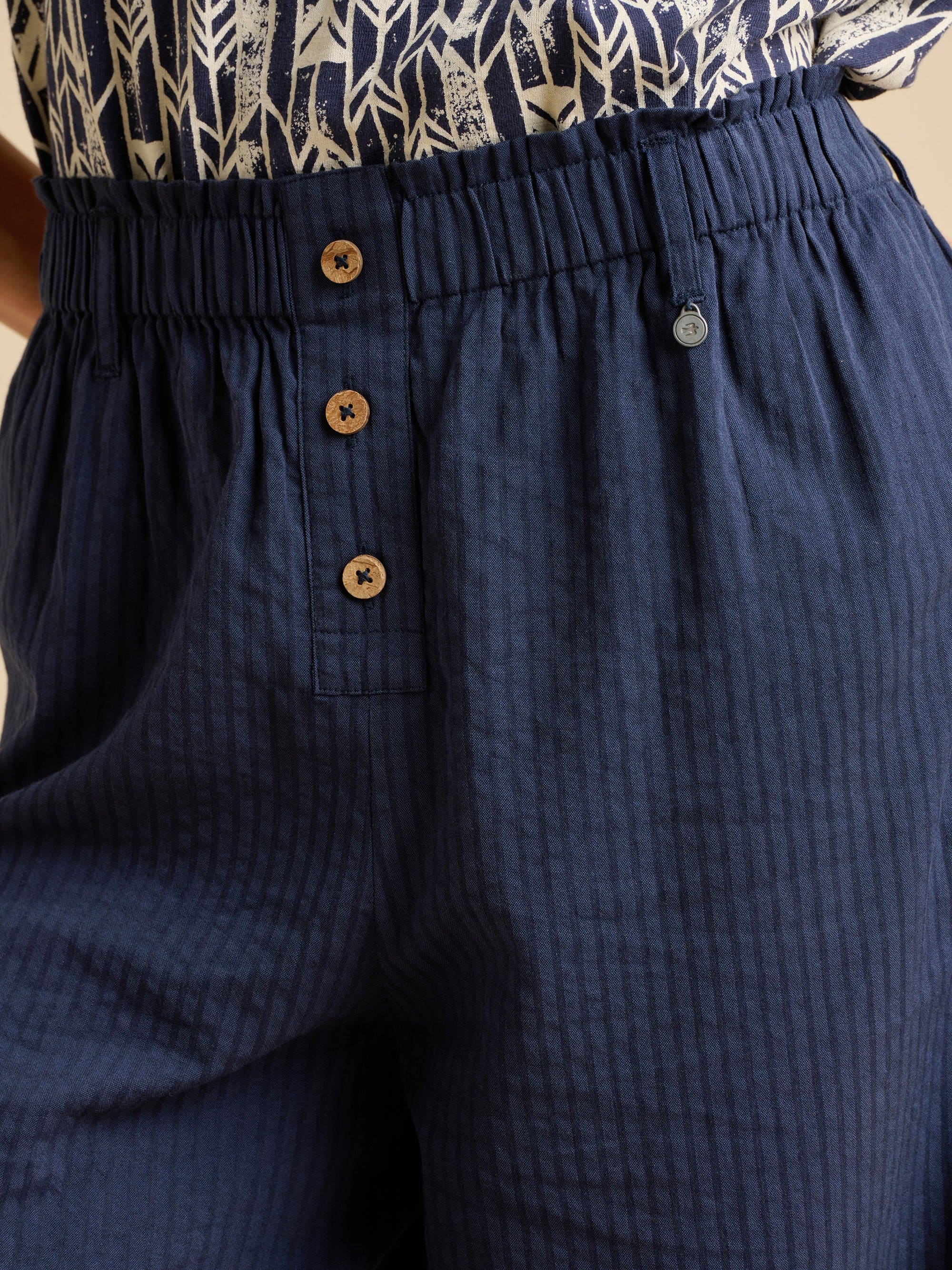 Close up of navy blue textured trousers with brown button details.