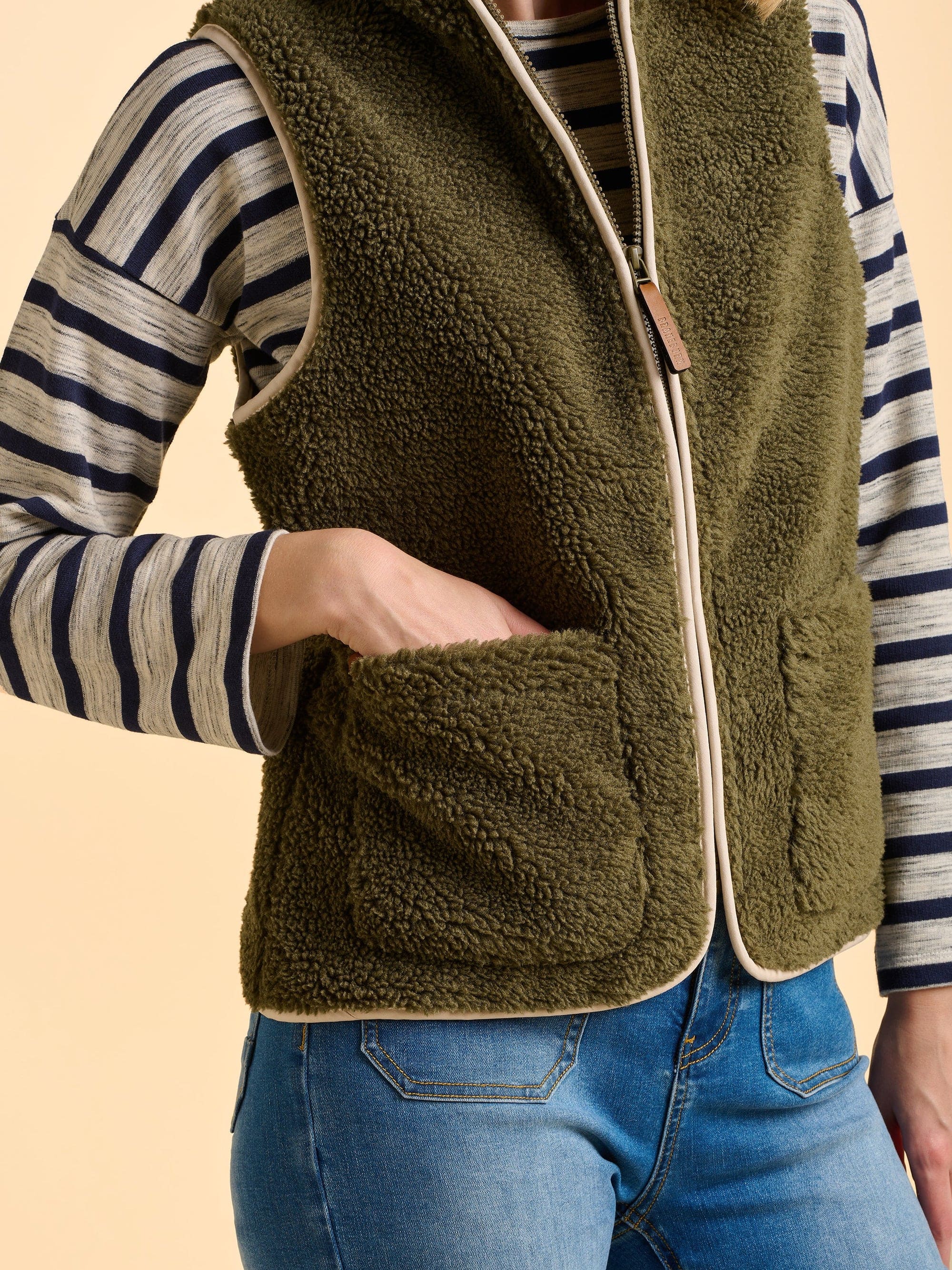 Woman wearing a green fleece gilet over a striped long sleeve top.